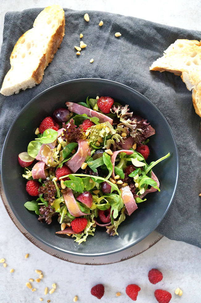 grüner Salat mit gemischten Salatblättern, Roastbeef, Himbeeren, Weintrauben und Honig-Senf Dressing, Pinienkernen und gerösteten Fladenbrot